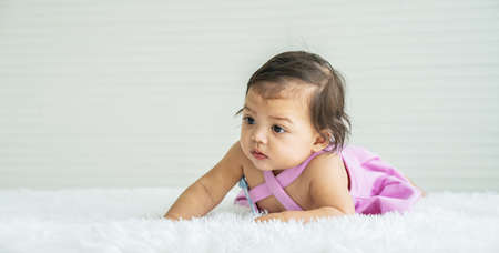 Childcare Concept. Portrait of cute little mixed race baby lying on white bed sheets at home. infant child crawling on bed in the bedroom. Selective focusの写真素材