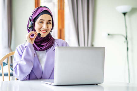 Portrait of muslim operator business woman working with headset and laptop computer, watch webinar listen online course communicate by conference video call, social distanceの写真素材
