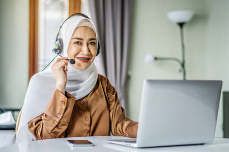 Portrait of muslim operator business woman working with headset and laptop computer, watch webinar listen online course communicate by conference video call, social distanceの写真素材