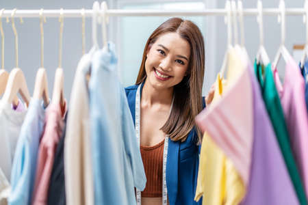 Beautiful woman business owner at fashion store choose clothes in the clothes rail, Fashion designer standing in order to repair, service for customers. Concept Profession Dressmaker designerの写真素材