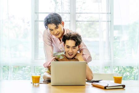 Young asian gay hugging and takes care of his boyfriend while working on his laptop at home, lgbt coupleの写真素材