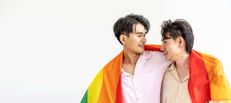 Guys spend time together at home, Portrait of Happy Asian gay couple embracing and showing their love under lgbt colorful rainbow flag. LGBT and love concept.の写真素材