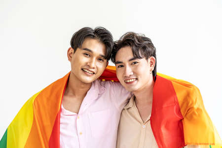 Guys spend time together at home, Portrait of Happy Asian gay couple embracing and showing their love under lgbt colorful rainbow flag. LGBT and love concept.の写真素材