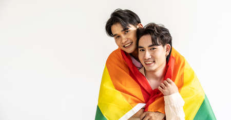 Guys spend time together at home, Portrait of Happy Asian gay couple embracing and showing their love under lgbt colorful rainbow flag. LGBT and love concept.の写真素材