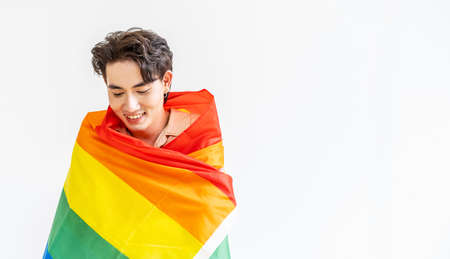 Portrait of transgender or gay man smiling in front of camera taking cover with lgbt flag on white background with copy space. People lifestyle fashion lgbtq conceptの写真素材