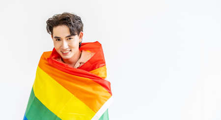 Portrait of transgender or gay man smiling in front of camera taking cover with lgbt flag on white background with copy space. People lifestyle fashion lgbtq conceptの写真素材