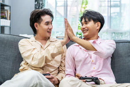 Two young males relax on weekend sit on couch enjoy console video game push buttons on controllers. Two Male Players spend free time together play online game having funの写真素材