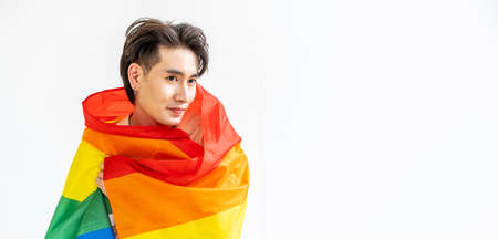 Portrait of transgender or gay man smiling in front of camera taking cover with lgbt flag on white background with copy space. People lifestyle fashion lgbtq conceptの写真素材