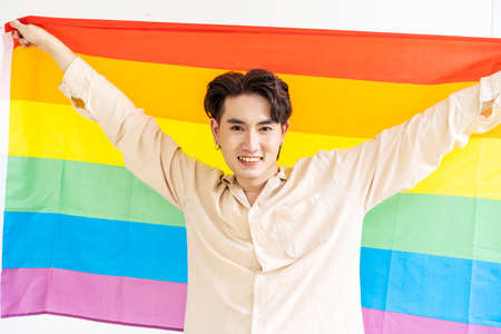 Portrait of transgender or gay man smiling in front of camera with pride rainbow flag isolated on white background with copy space. People lifestyle fashion lgbtq conceptの写真素材