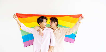 Portrait of Happy gay couple showing their love with rainbow flag. holding each other and holding up an LGBTQ flag, They are laughing, LGBT and love concept.の写真素材