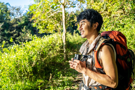 Young travel man relax and enjoy in the Woods, holds binoculars during a camping trip against blue vivid sky.の写真素材