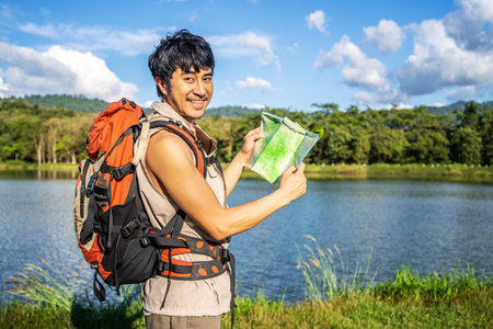 Young asian attractive male tourists looking for map in forest, Lost hiker male with backpacks reading travel map, Navigating and looking for directions in pine forest. Trekking concept.の写真素材