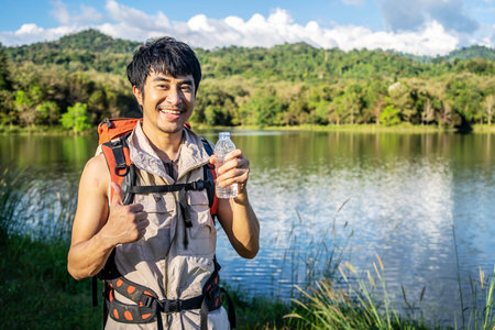 Handsome young asian male traveler resting in nature, holding a bottle with water in nature. Natural resource, Young man living active life, fun and smile.の写真素材