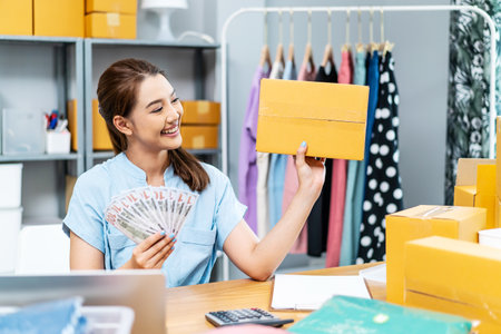 Entrepreneurs Small Business SME freelance, young Asian woman holding US dollars lot of money with box, she is happy and proud smile work at home, online marketing packing box delivery, online salesの写真素材