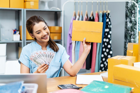 Entrepreneurs Small Business SME freelance, young Asian woman holding US dollars lot of money with box, she is happy and proud smile work at home, online marketing packing box delivery, online salesの写真素材