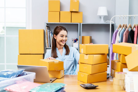 Portrait young attractive asia female owner startup business using computer laptops work happy with carton box at home prepare delivery to customers, procurement, omnichannel ecommerce online conceptの写真素材