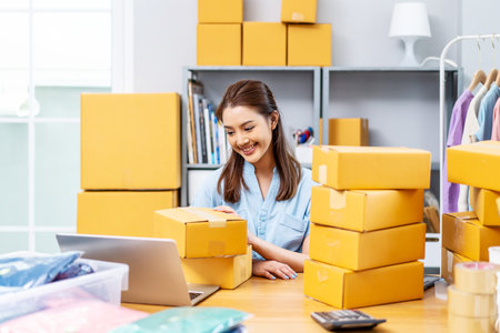 Portrait young attractive asia female owner startup business using computer laptops work happy with carton box at home prepare delivery to customers, procurement, omnichannel ecommerce online conceptの写真素材