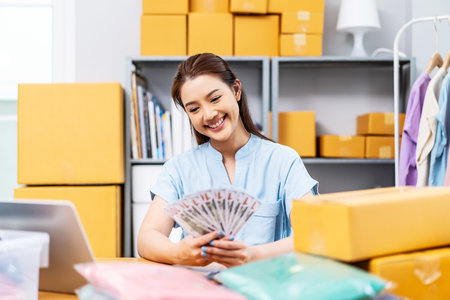 Entrepreneurs Small Business SME freelance, young Asian woman holding US dollars money lot of money happy and proud smile work at home, online marketing packing box delivery, online salesの写真素材