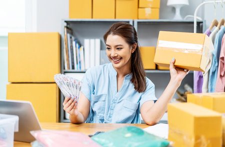 Entrepreneurs Small Business SME freelance, young Asian woman holding US dollars lot of money with box, she is happy and proud smile work at home, online marketing packing box delivery, online salesの写真素材