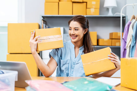 Entrepreneurs Small Business SME freelance, young Asian woman holding parcel box and sitting on chair, she is happy smile work at home, online marketing packing box delivery, online salesの写真素材