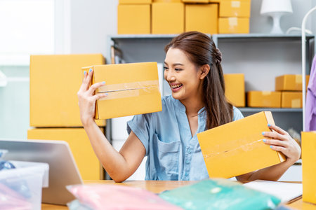 Entrepreneurs Small Business SME freelance, young Asian woman holding parcel box and sitting on chair, she is happy smile work at home, online marketing packing box delivery, online salesの写真素材