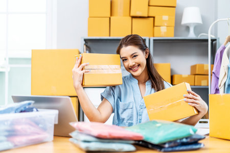 Entrepreneurs Small Business SME freelance, young Asian woman holding parcel box and sitting on chair, she is happy smile work at home, online marketing packing box delivery, online salesの写真素材