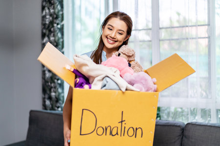 Donation Concept. Happy volunteer asian woman holding a Donate Box with full of toy doll, She working at charity center.の写真素材