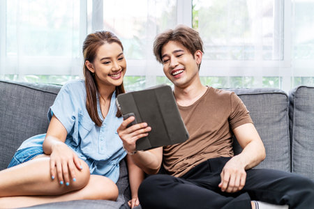 Portrait of an happy couple in love using a tablet, looking at digital computer tablet screen, relaxing on comfortable couch. Loving couple shopping online in internet store.の写真素材