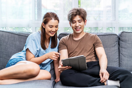Portrait of an happy couple in love using a tablet, looking at digital computer tablet screen, relaxing on comfortable couch. Loving couple shopping online in internet store.の写真素材