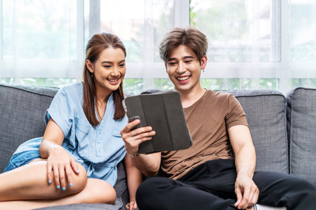 Portrait of an happy couple in love using a tablet, looking at digital computer tablet screen, relaxing on comfortable couch. Loving couple shopping online in internet store.の写真素材