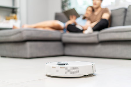 Young couple resting on the couch while robotic vacuum cleaner doing its work at home. Household robots, Smart home conceptの写真素材