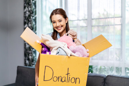 Donation Concept. Happy volunteer asian woman holding a Donate Box with full of toy doll, She working at charity center.の写真素材
