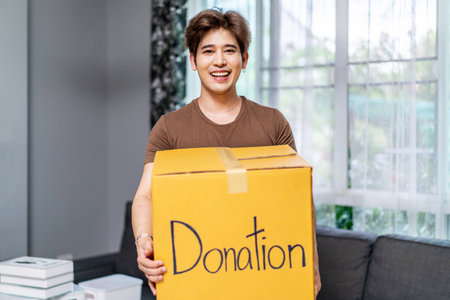 Donation Concept. Happy volunteer asian man holding a Donate Box for Giving, Smiling male working at charity center.の写真素材