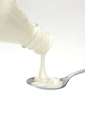 Thick white liquid being poured into a spoon from a glass bottleの写真素材