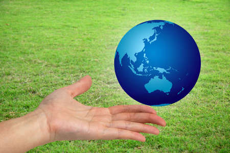 Hand holding a the world with a green grassy field in the bckgroundの写真素材