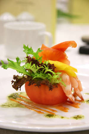 Appetizer of shrimp and mango in a carved out tomato and a dash of different lettuce leavesの写真素材