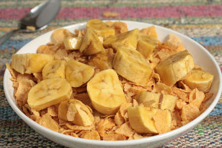Bowl of cornflakes with banana slices on a brownish beige mat