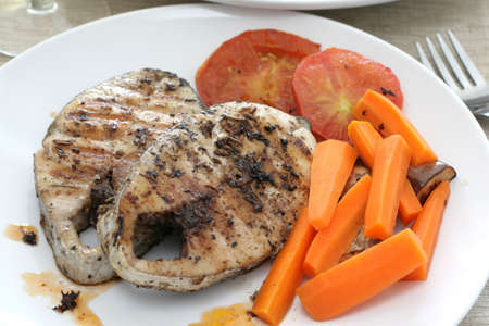 Pan seared mackerel served with carrots, sliced tomatoes and white wineの写真素材