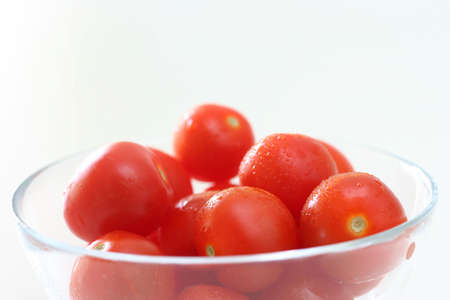 Cherry tomatoes in a transparent glass bowl on a white table-topの写真素材