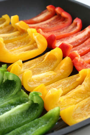 Colorful rows of green, yellow and red capsicum strips prepared for cooking on a pan