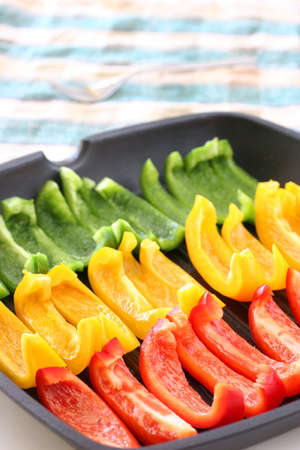 Colorful rows of green, yellow and red capsicum strips prepared for cooking on a pan
