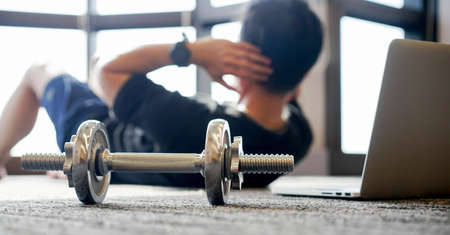 close up dumbbell with young man in sit-up pattern on the floor to workout with online trainer course from website for quarantine lifestyle and healthy conceptの写真素材