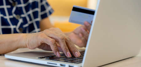 close up senior woman hand using keyboard laptop and holding credit card to paying bills from...