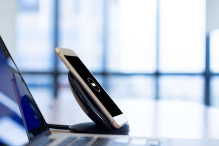 close up on smartphone charging on wireless charger equipment of office table for technology conceptの写真素材