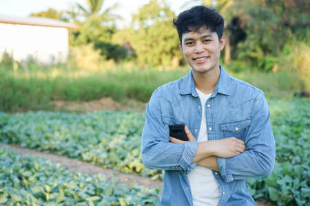 close up young asian farmer (owner) man crossing arm and standing at agricultural field in the...