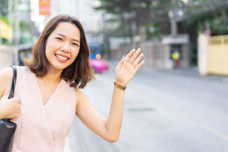 close up young employee woman raising hand to call on taxi car to get on for go to work in the rush time , city life conceptの写真素材