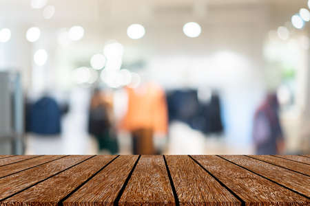 abstract blur clothing store inside shopping mall with wood tabletop for show , promote promotion on...