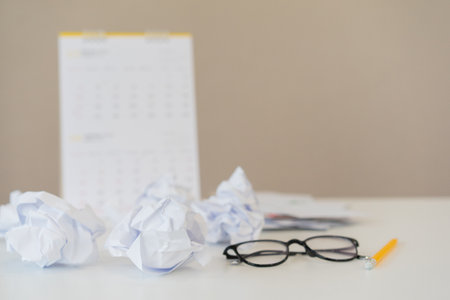 close up crumpled paper ball with eyeglasses, pen and calendar on the table after rejection project for deadline of working conceptの写真素材