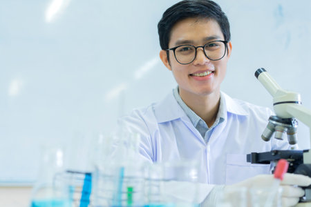 close up young asian scientist sitting with microscope to research or record and analyze about scientific experiment result at laboratory for healthcare and pharmaceutical conceptの写真素材