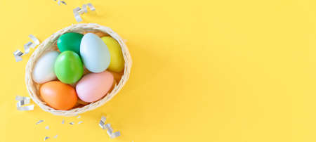 Colorful Easter eggs in a basket on a yellow background. Happy Easter concept.